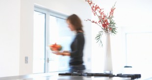Woman carrying bowl of fruit in kitchen, side view (blurred motion)