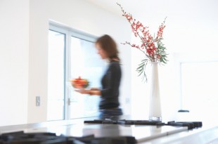 Woman carrying bowl of fruit in kitchen, side view (blurred motion)